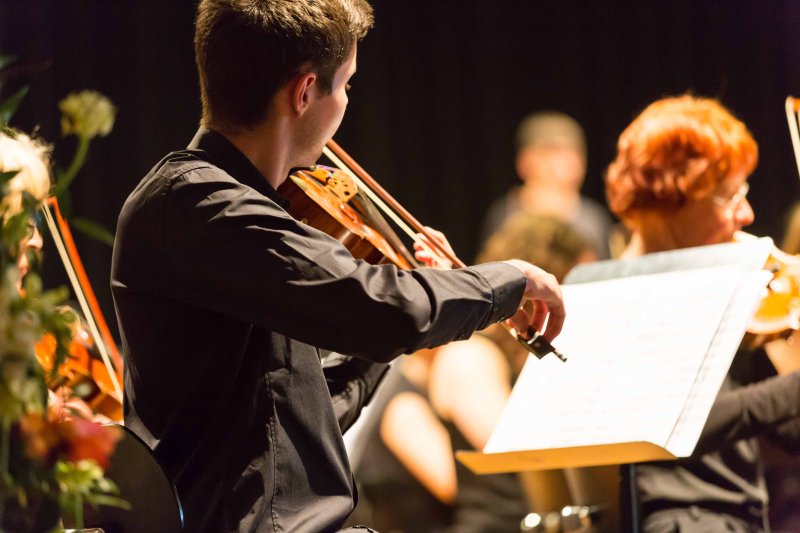 Konzert: Geiger spielt Violine im Orchester. Klassische Musik, Musiker, Bühne.