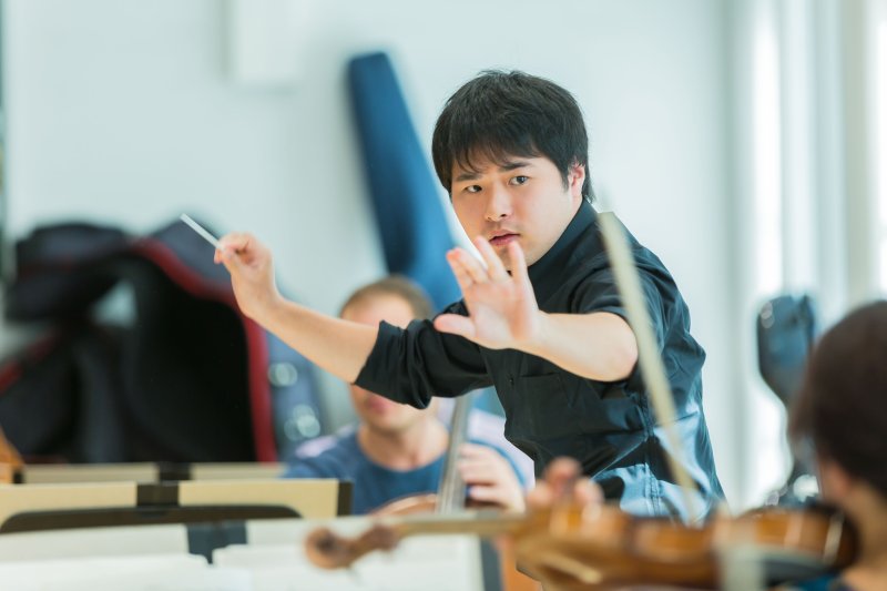 Dirigent leitet Orchesterprobe. Asiatischer Musiker mit Taktstock. Konzert, Musik.